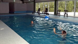 An indoor swimming pool with clear water, surrounded by lounge chairs and a covered roof structure. - Les chalets de la héronnière (Chef-Boutonne)