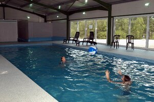 Une piscine intérieure à l’eau claire, entourée de chaises longues et dotée d’une structure de toit abritée.
