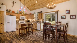 A kitchen with wooden cabinets, a white refrigerator, a microwave, and a dining area with wooden chairs. - Custom Home with Two Private Master Suites and Heated Garage (Angel Fire)