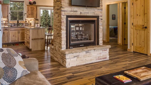 A spacious living room with a stone fireplace, wooden ceiling, and a television mounted above it. - Custom Home with Two Private Master Suites and Heated Garage (Angel Fire)