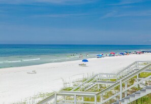A beach with white sand, a staircase leading down to the shore, and a clear blue sky.