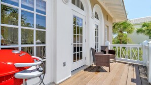 Eine überdachte Terrasse im Freien mit einem roten Grill, Korbmöbeln und weißen Geländern.
