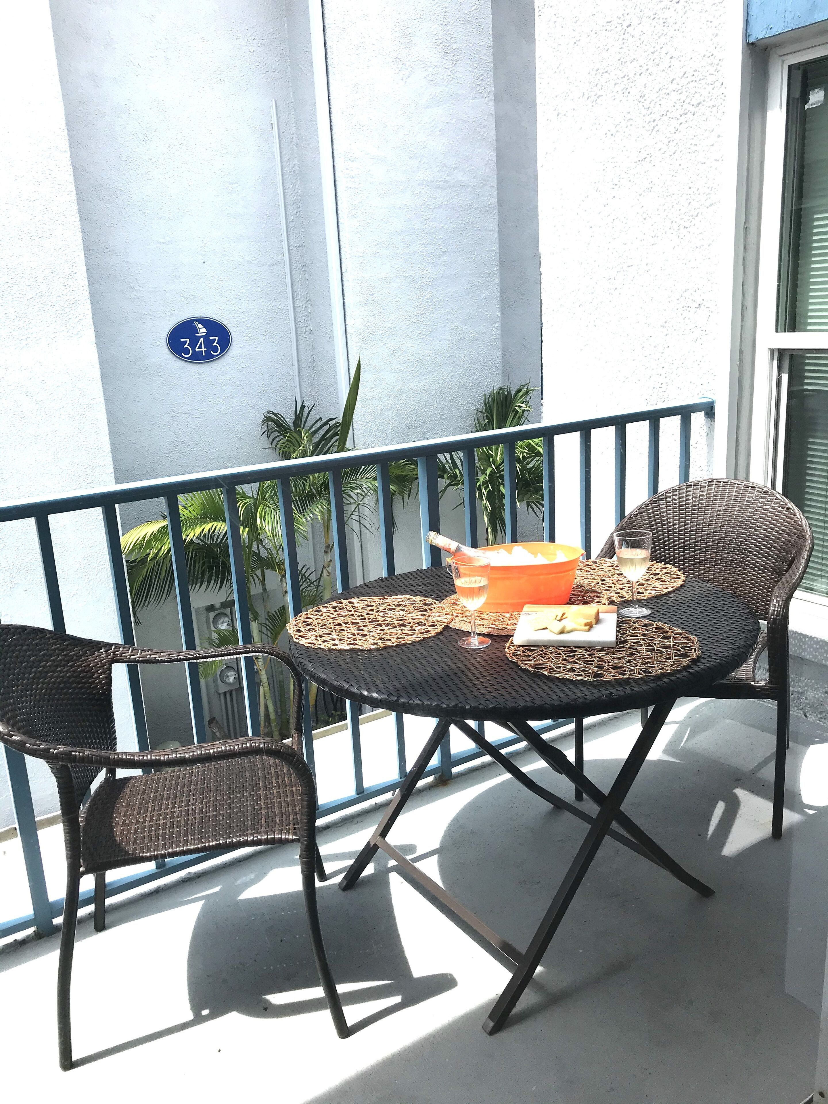 A balcony with a table set for two, featuring wicker chairs and a small orange table.