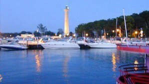 Un puerto deportivo con barcos amarrados, un faro destacado al fondo y un tranquilo ambiente vespertino.