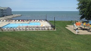 Una piscina con vista al mar, rodeada de césped y un edificio al fondo.