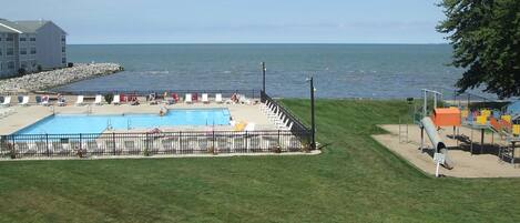 A swimming pool with a view of the sea, surrounded by a grassy area and a building in the background.