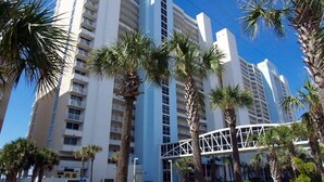 A high-rise hotel with multiple floors, palm trees, and a pedestrian bridge. - 4th floor@Majestic! 3br!2 King beds+Triple Bunk! Gym/weight room access included (Panama City Beach)