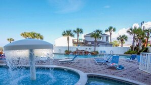 A pool area with a water fountain, lounge chairs, and palm trees. - 4th floor@Majestic! 3br!2 King beds+Triple Bunk! Gym/weight room access included (Panama City Beach)