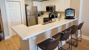 A modern kitchen with a central island, bar stools, stainless steel appliances, and white cabinetry. - 4th floor@Majestic! 3br!2 King beds+Triple Bunk! Gym/weight room access included (Panama City Beach)