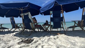 Een strand met rijen blauwe strandstoelen en parasols, waarvan sommige bezet zijn, onder heldere luchten.