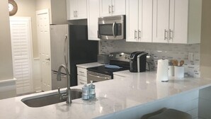 Een moderne keuken met witte kastjes, roestvrijstalen apparatuur en een groot eiland met barstoelen.