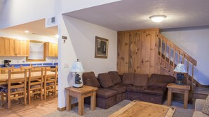A cozy living room with a wooden staircase, a brown leather sofa, a wooden coffee table, and a dining area with wooden chairs and a table. - Perfect family space. Lots of room. Easy drive to New River Gorge National Park. (Ghent)