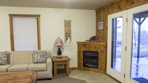 A cozy living room with a wooden fireplace, a sofa, a coffee table, and a door leading outside. - Perfect family space. Lots of room. Easy drive to New River Gorge National Park. (Ghent)