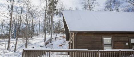 Una cabaña de madera con un porche cubierto de nieve y vista a un bosque nevado.
