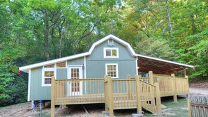A two-story house with a porch and a fenced deck, surrounded by trees. - Cozy Forest Tiny Cabin • Hot Tub • Fire Pit • Pets Welcome • Near NOC & GSMR (Almond)