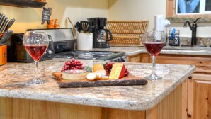 A kitchen counter with two glasses of red wine, a cheese board with various cheeses and grapes, and a coffee maker. - Cozy Forest Tiny Cabin • Hot Tub • Fire Pit • Pets Welcome • Near NOC & GSMR (Almond)