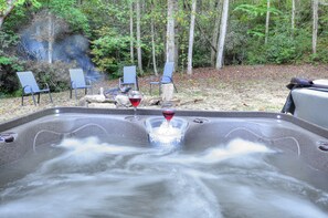 Ein Whirlpool mit einem klaren Glas und einem roten Getränk, umgeben von Stühlen und einem bewaldeten Hintergrund.