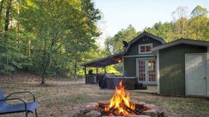 A backyard with a stone fire pit, outdoor seating, a hot tub, and a covered patio area. - Cozy Forest Tiny Cabin • Hot Tub • Fire Pit • Pets Welcome • Near NOC & GSMR (Almond)