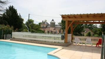 A swimming pool with a wooden pergola and white chairs.