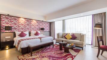 Een moderne hotelkamer met een groot bed, een bank, een stoel, een klein tafeltje en een groot raam met gordijnen.