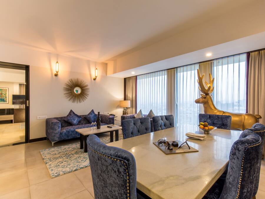 A modern hotel room with a dining area, a sofa set, a large mirror, and a decorative deer head.