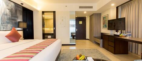 Una habitación de hotel con cama, escritorio, televisor y zona de comedor con frutero.