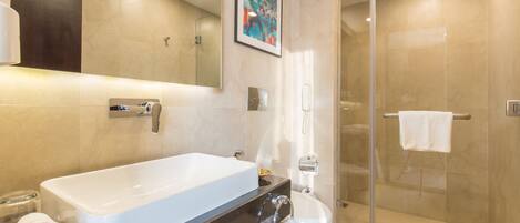 Un baño moderno con una bañera blanca grande, ducha con cerramiento de vidrio y pared revestida de mármol.