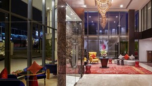 Un vestíbulo moderno con una lámpara de araña grande, zona de estar con sofás y sillones, y ventanas amplias que dan vistas a la calle.