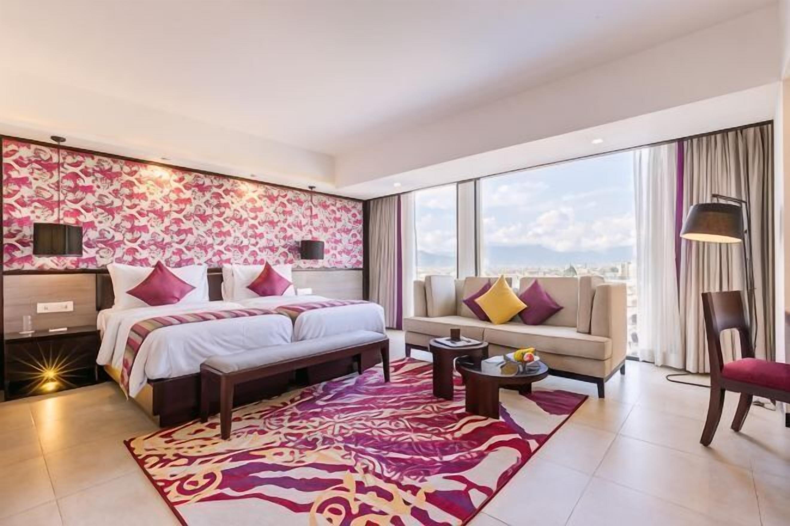 A modern hotel room with a large bed, a sofa, a small table, and a city view.