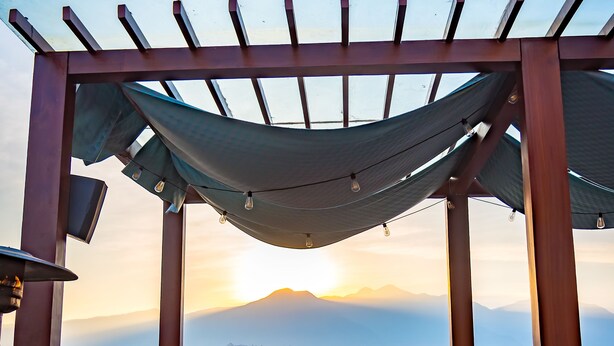 Una terraza en la azotea con una pérgola, zona de estar y vistas a la ciudad y montañas.