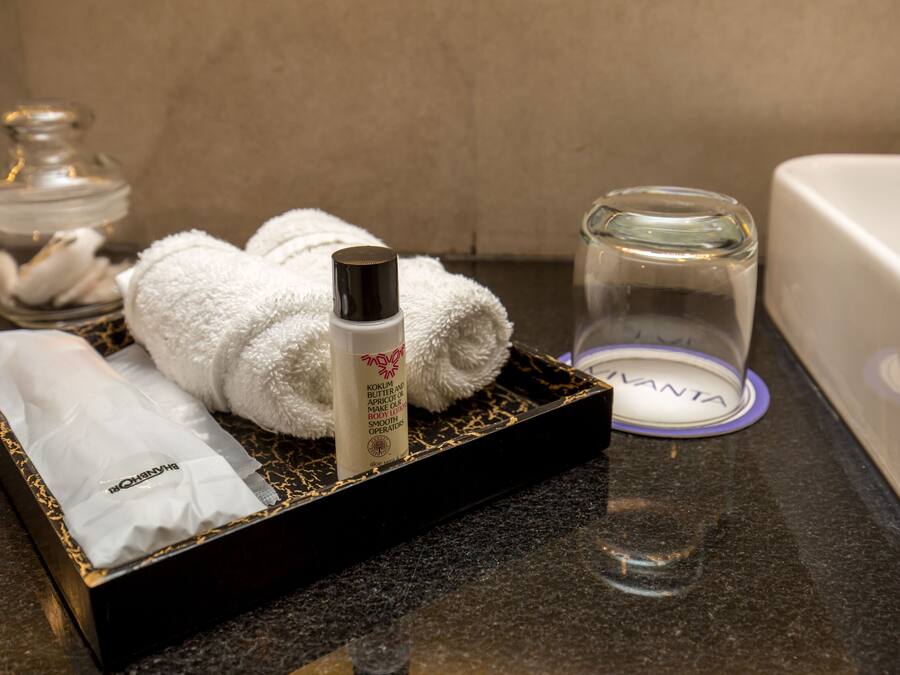 A bathroom with a black tray holding a white towel, a bottle of lotion, a glass of water, and a glass jar.