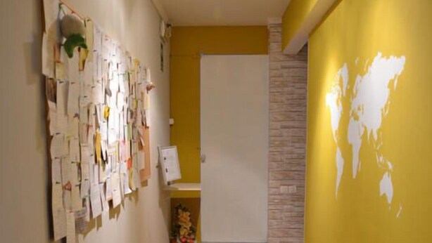 A hallway with wooden flooring, a bulletin board on the left, and a yellow wall with a map on the right. - Leonardo Tourist House (Florence)