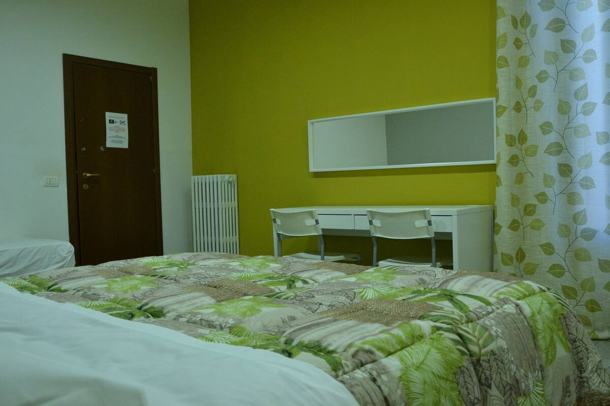 A room with a bed, a desk, a chair, a mirror, and a radiator.