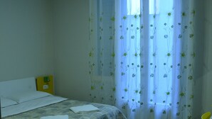 A bedroom with a bed, a nightstand, and a window with floral curtains. - Leonardo Tourist House (Florence)
