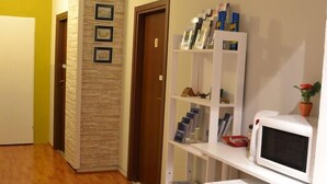 A hallway with wooden flooring, a white refrigerator, a microwave, and a bookshelf with books and decorative items. - Leonardo Tourist House (Florence)