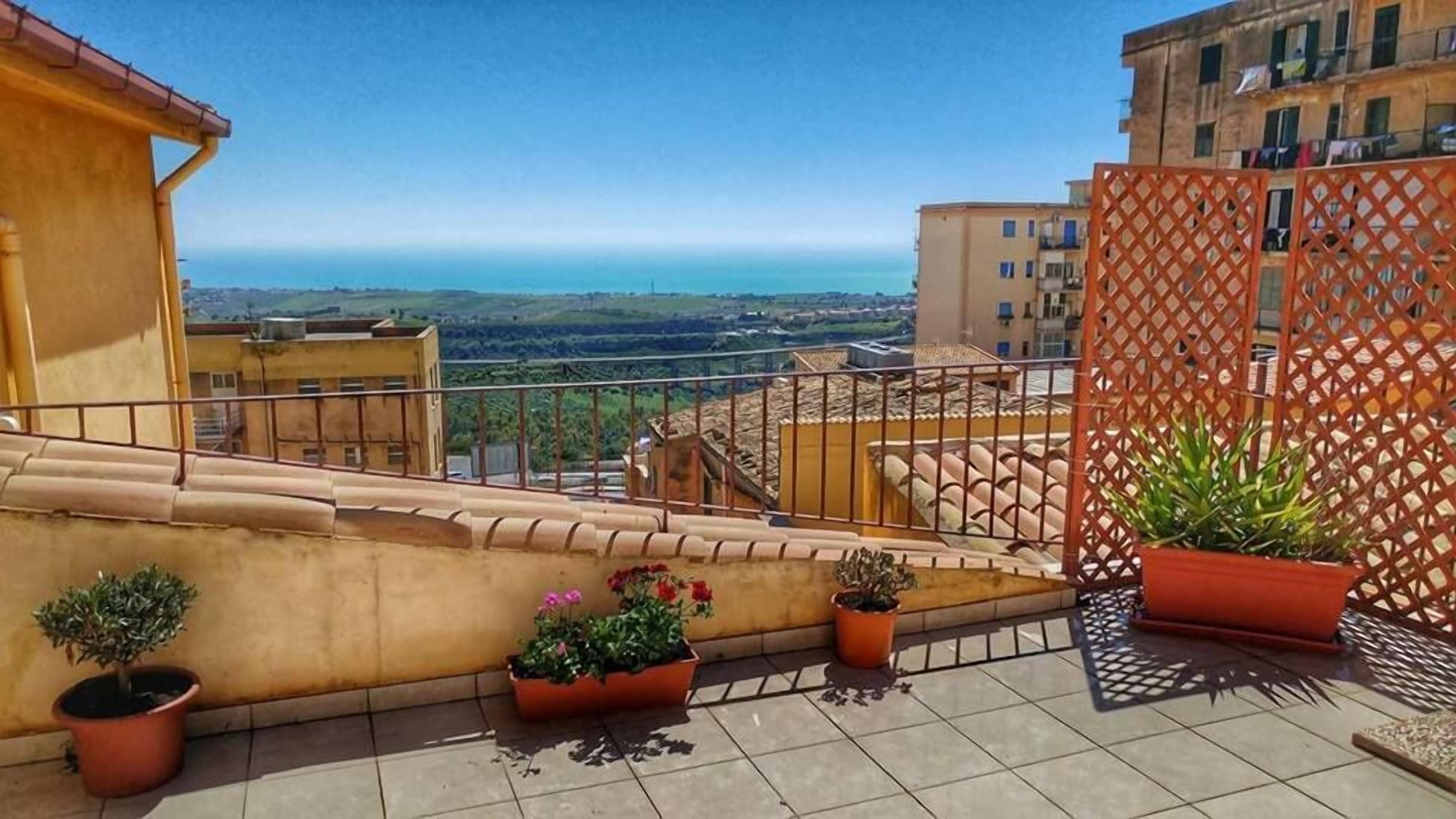 A rooftop terrace with potted plants, a view of the sea, and surrounding buildings.