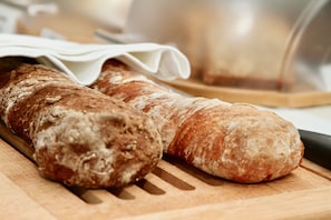 Two loaves of bread on a wooden cutting board. - Hotel Bartmanns Haus (Dillenburg)
