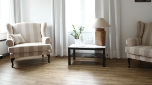 Una habitación con un sillón a rayas, una mesita con una lámpara y un sofá.