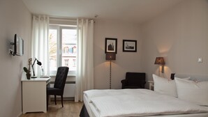 Una habitación de hotel con cama, escritorio, silla y dos cuadros en la pared.
