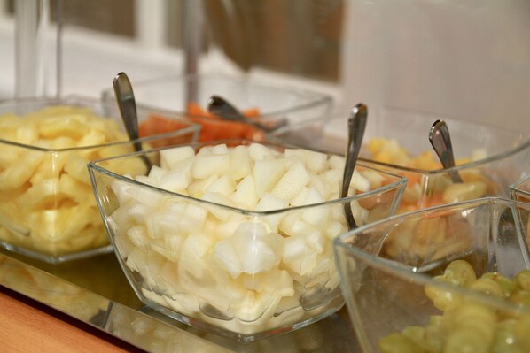 Un bufé con diversos alimentos en recipientes de vidrio transparente, incluyendo patatas en cubos y otras verduras.