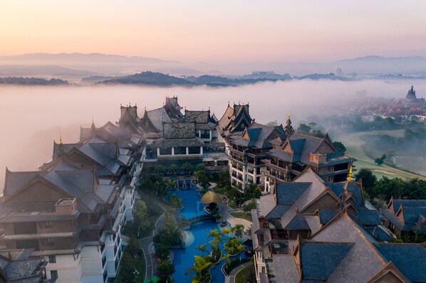 A traditional architectural hotel with multiple buildings, a swimming pool, and a view of the surrounding landscape.