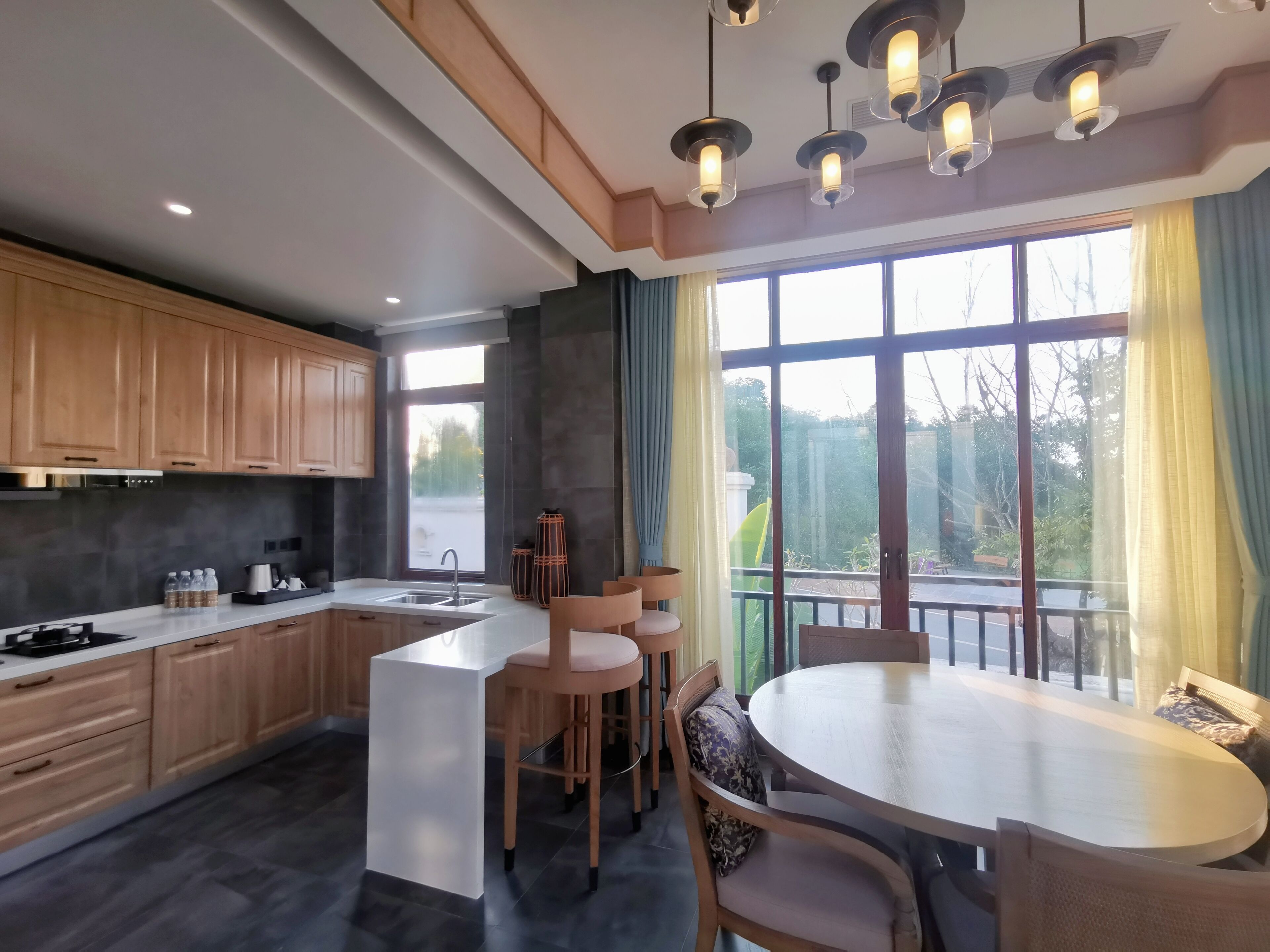 A modern kitchen with wooden cabinets, a central island, and a dining area with a round table and chairs.