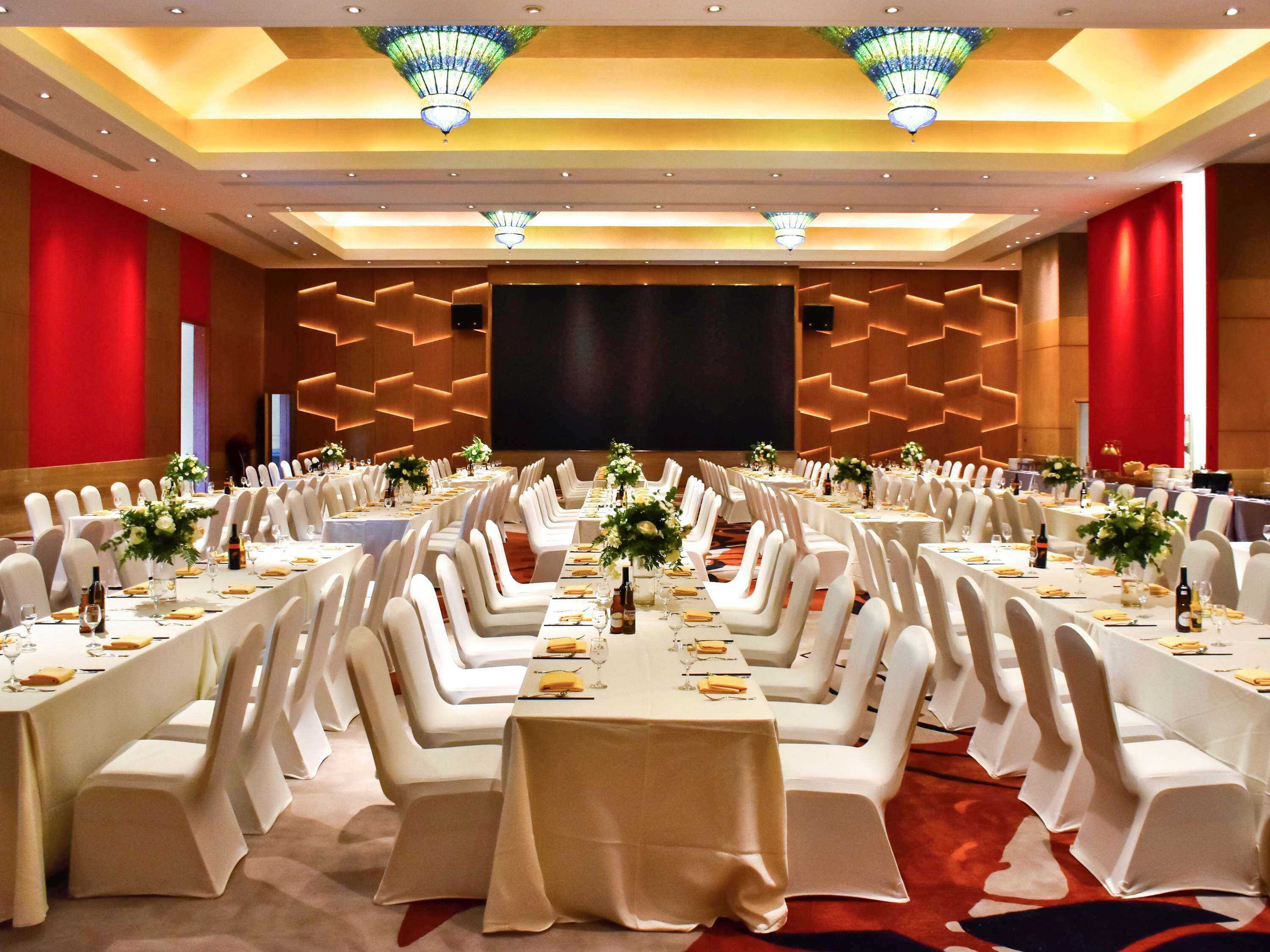 A conference room with multiple tables, white chairs, and a large screen.
