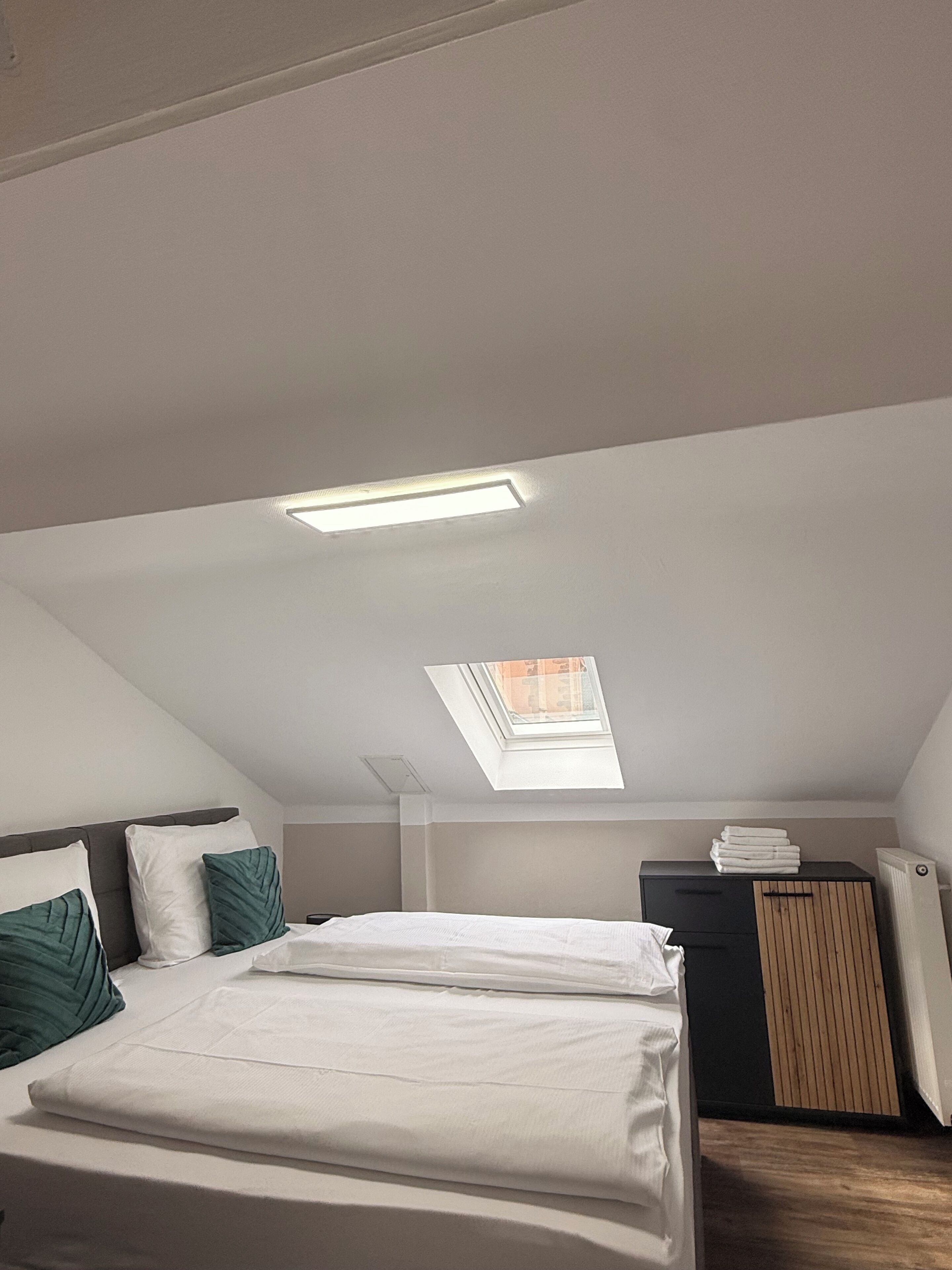 Ein Schlafzimmer mit Dachfenster, einem Bett mit weißer Bettwäsche, einem Schminktisch und einer Heizung.