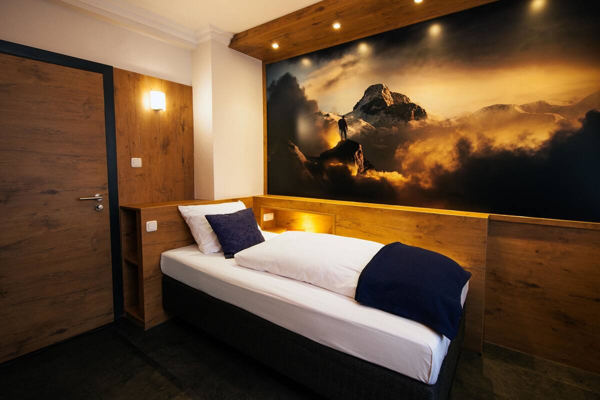 Habitación de hotel con cama, cabecero de madera, un gran mural en la pared con una montaña y una puerta de madera.
