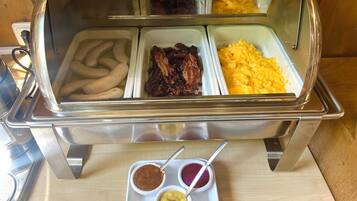 Un bufé con diversos alimentos, incluyendo salchichas, tocino y huevos revueltos.