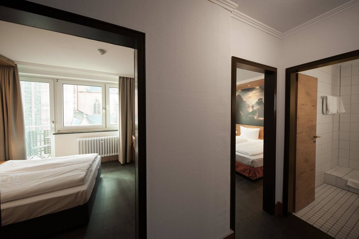 Una habitación de hotel con cama, ventana con cortinas, radiador y zona de ducha.