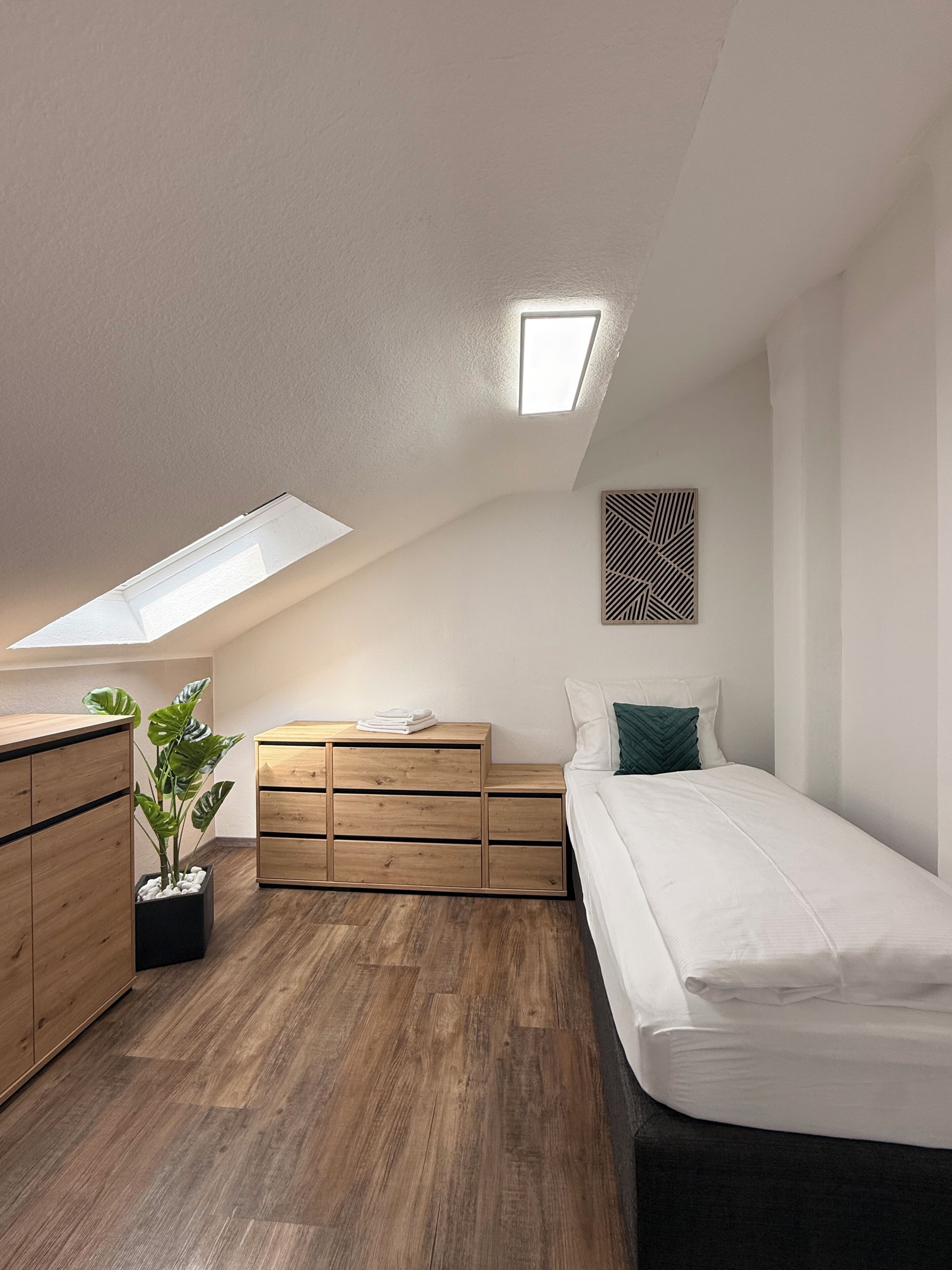 A bedroom with a skylight, wooden furniture, a bed, and a potted plant.