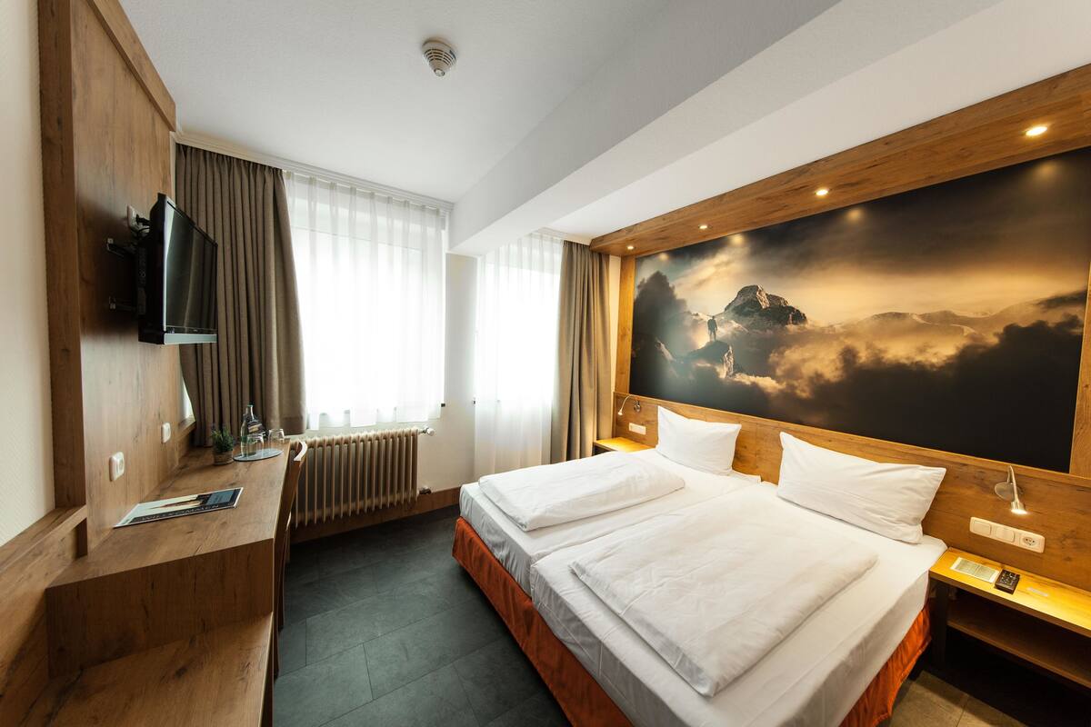 Una habitación de hotel con cama, escritorio, televisión y un mural grande en la pared.