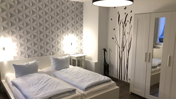 A modern bedroom with a large bed, two bedside tables, a wall-mounted light fixture, and a wardrobe. - Gasthaus Zum Schwan (Dillenburg)